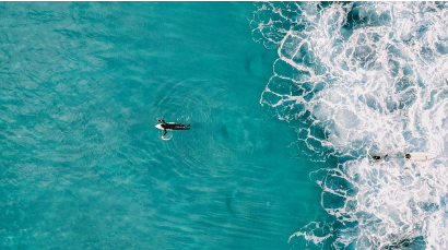 Surfista en el mar visto desde un dron, aguas turquesas y olas rompiendo
