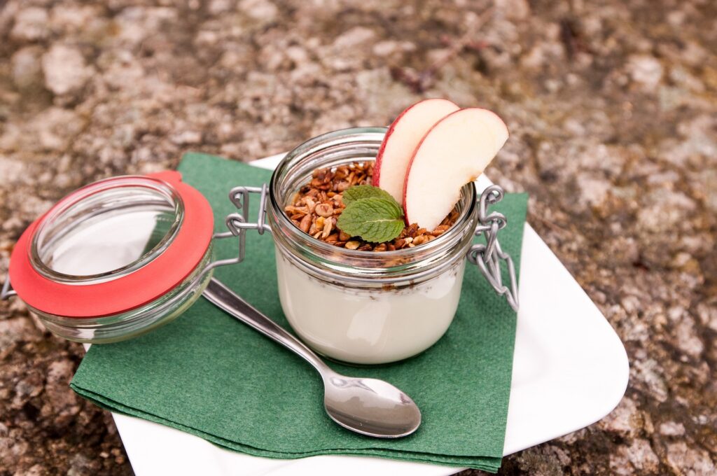 Tarro de cristal con yogur, granola, menta fresca y láminas de manzana, snack saludable para llevar a la playa