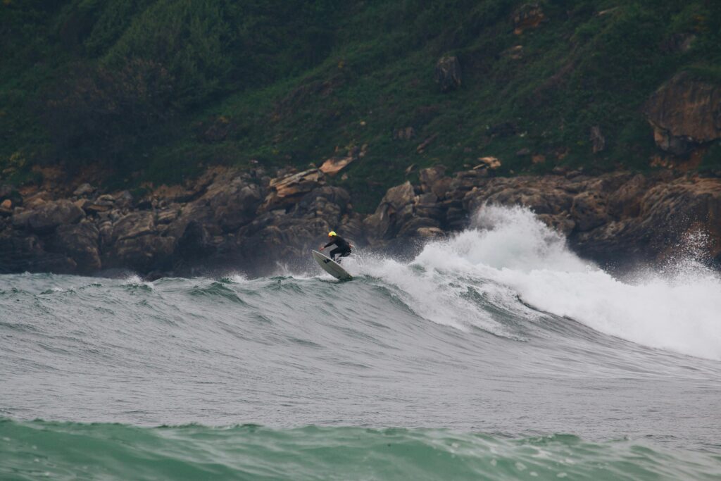 Surfista dominando el pico de una ola cerca de un acantilado rocoso