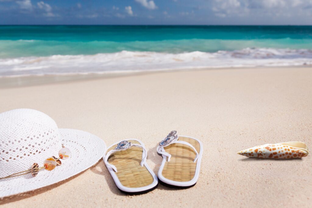 Sombrero de paja, chanclas y conchas en la arena de la playa